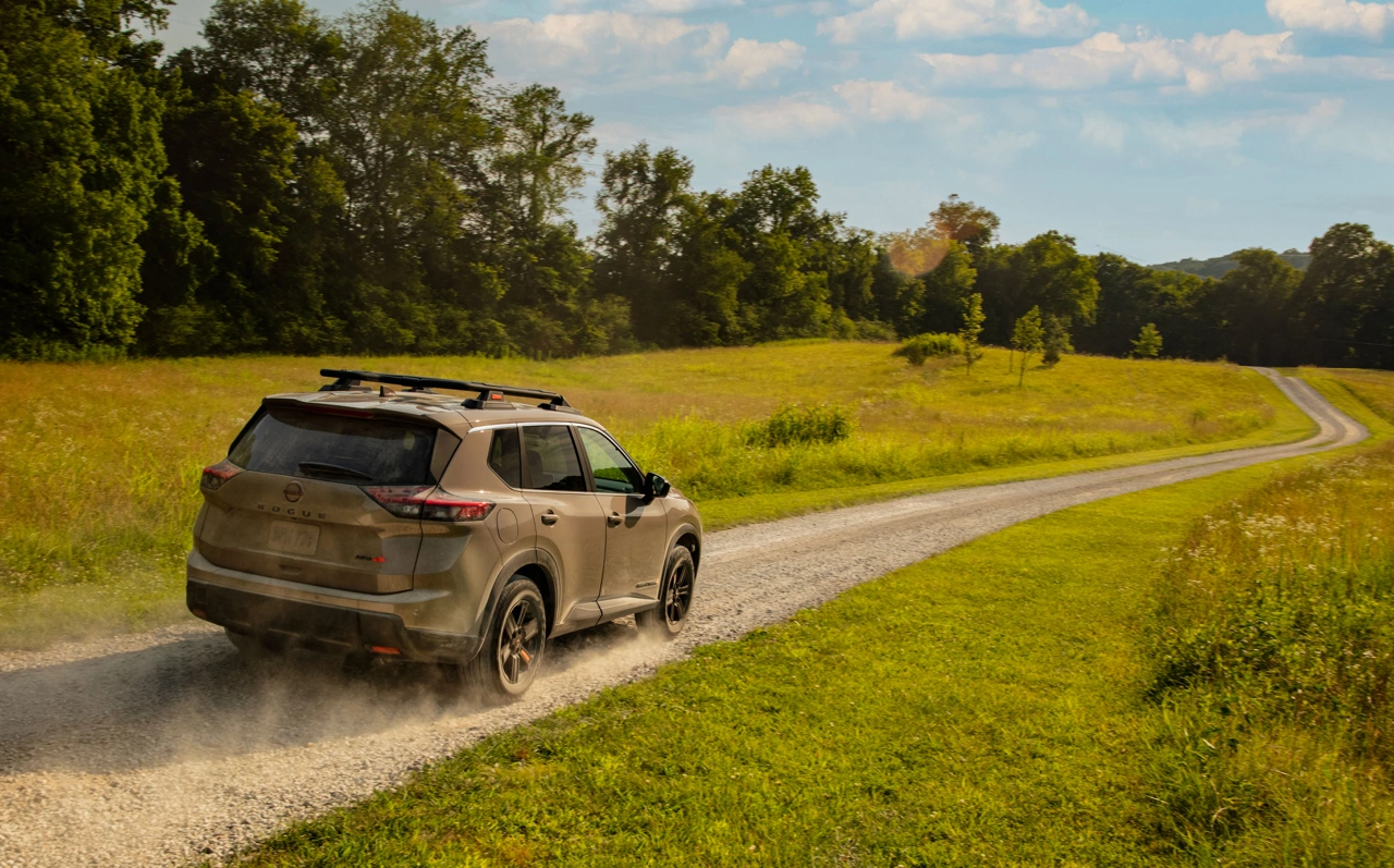 2026 Nissan Rogue Rock Creek seen from the rear on a country road to present its design.