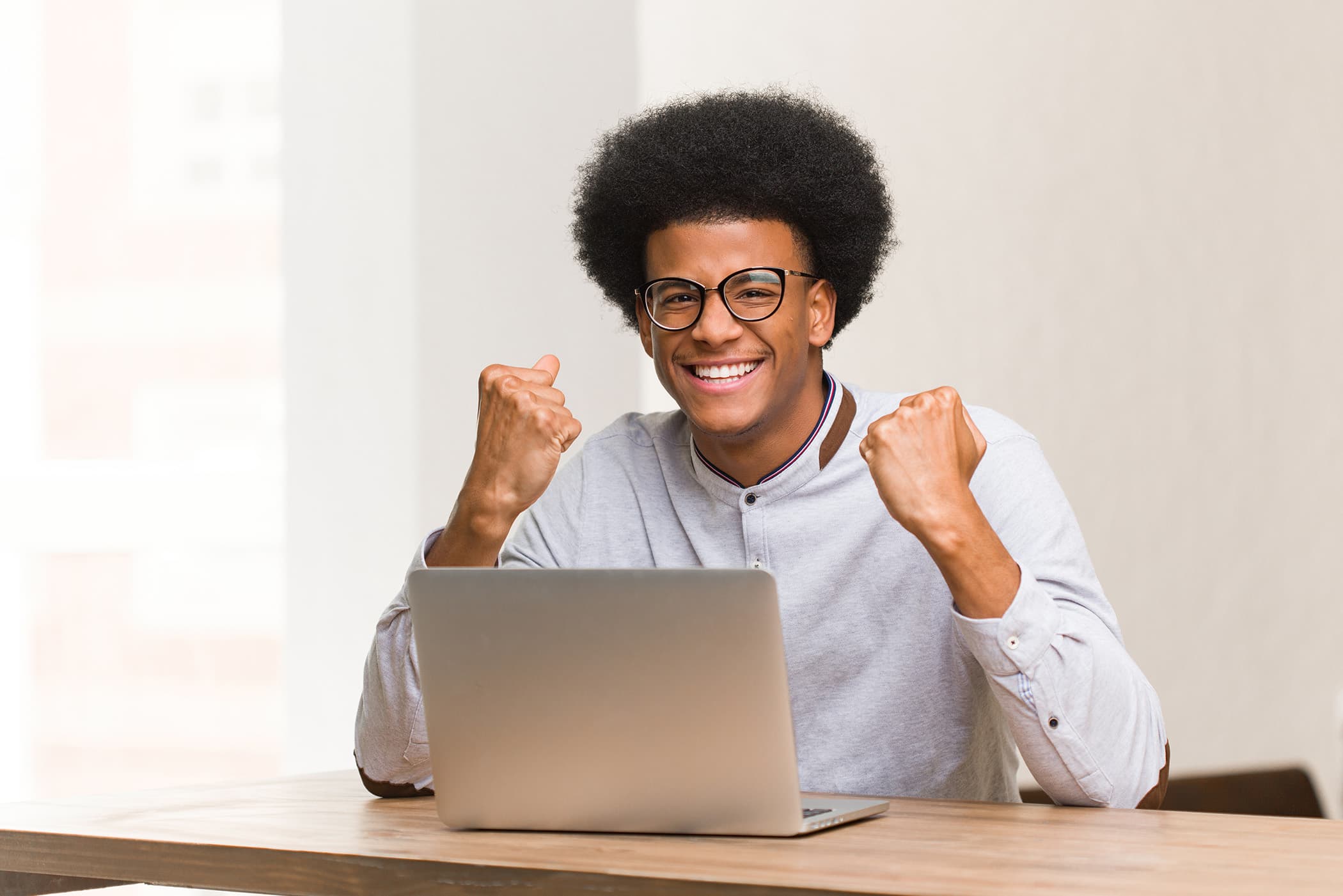 Image of a super happy guy smiling with his hands up, sitting at a desk with a laptop qualifying for an auto loan.